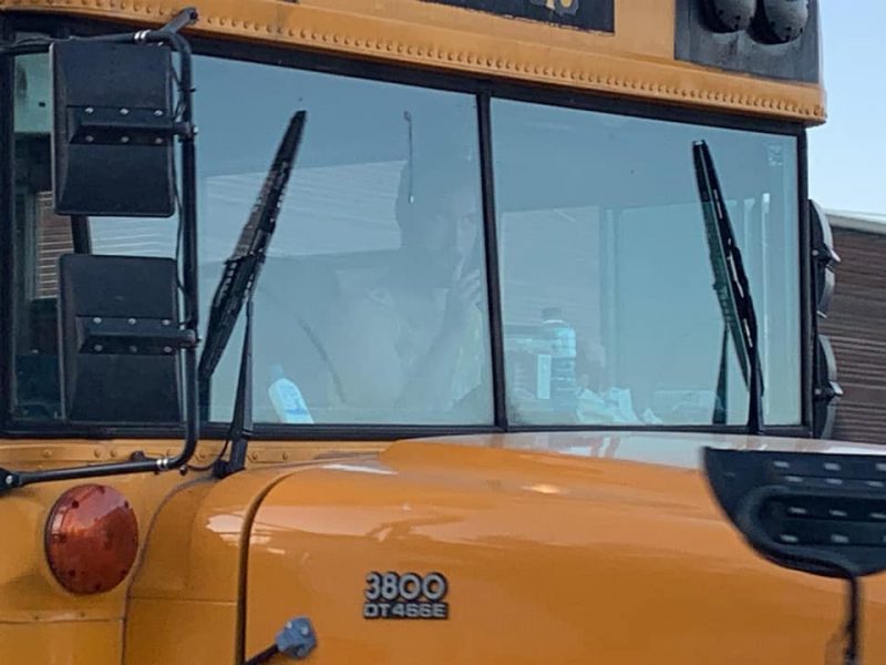 close up of Andrew Loudon in the driver's seat of the school bus wearing a yellow dress