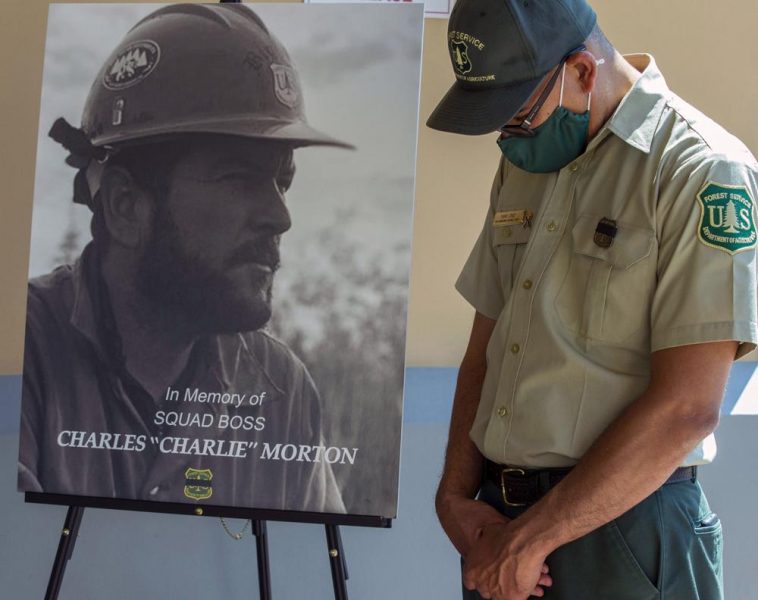 A firefighter lowers his head next to a memorial photograph of Charles Morton, a U.S. Forest Service firefighter killed in the line of duty on the El Dorado Fire.