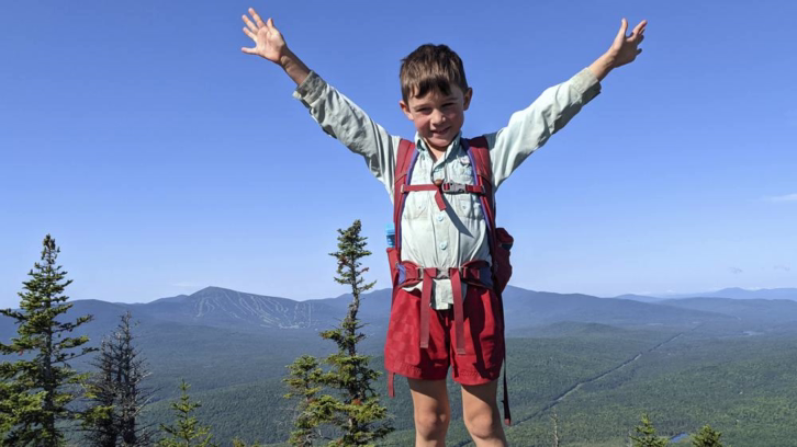 5-year-old hiker Harvey Sutton raising his arms on a mountain top in Bigelow Preserve, Maine, while hiking the Appalachian Trail with his Mom and Dad