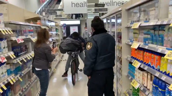 The shoplifter seen riding his bike down the aisle with a garbage bag full of stolen goods as a woman and a security guard watch