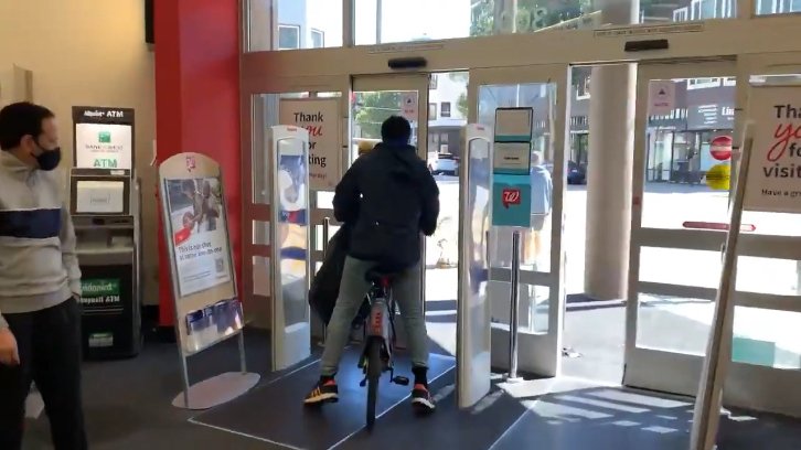 The shoplifter rides out on his bike through the store's automatic front door