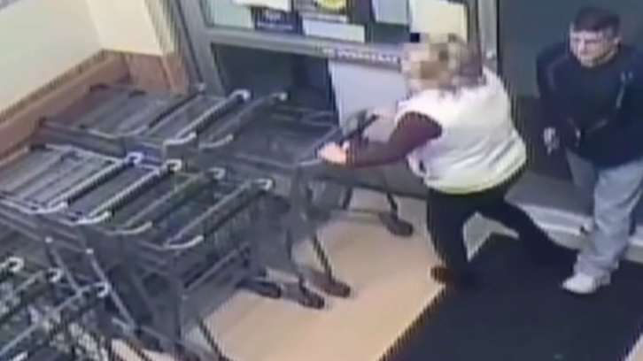 woman putting away shopping cart as man approaches her behind with something in his right hand