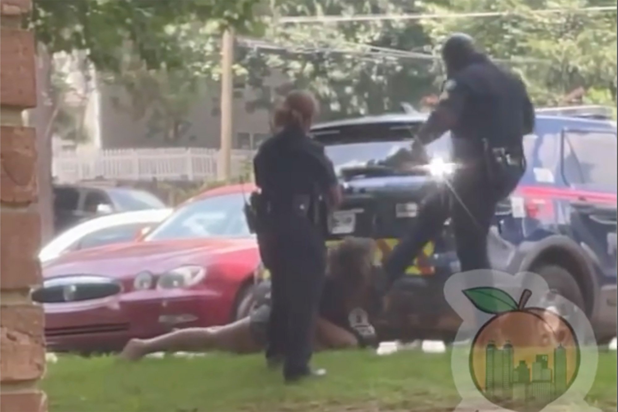 still from clip showing one police officer kicking the woman, who is lying face-down with her hands cuffed behind her back