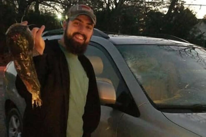 North Carolina man Stuart Barrow standing next to the car and smiling while holding the flying catfish