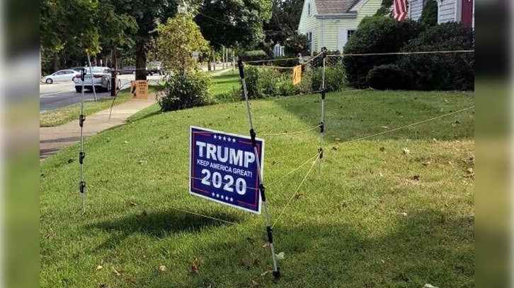 An electric fence surrounds a campaign sign for President Donald Trump in John Oliveira's yard in New Bedford, Mass.