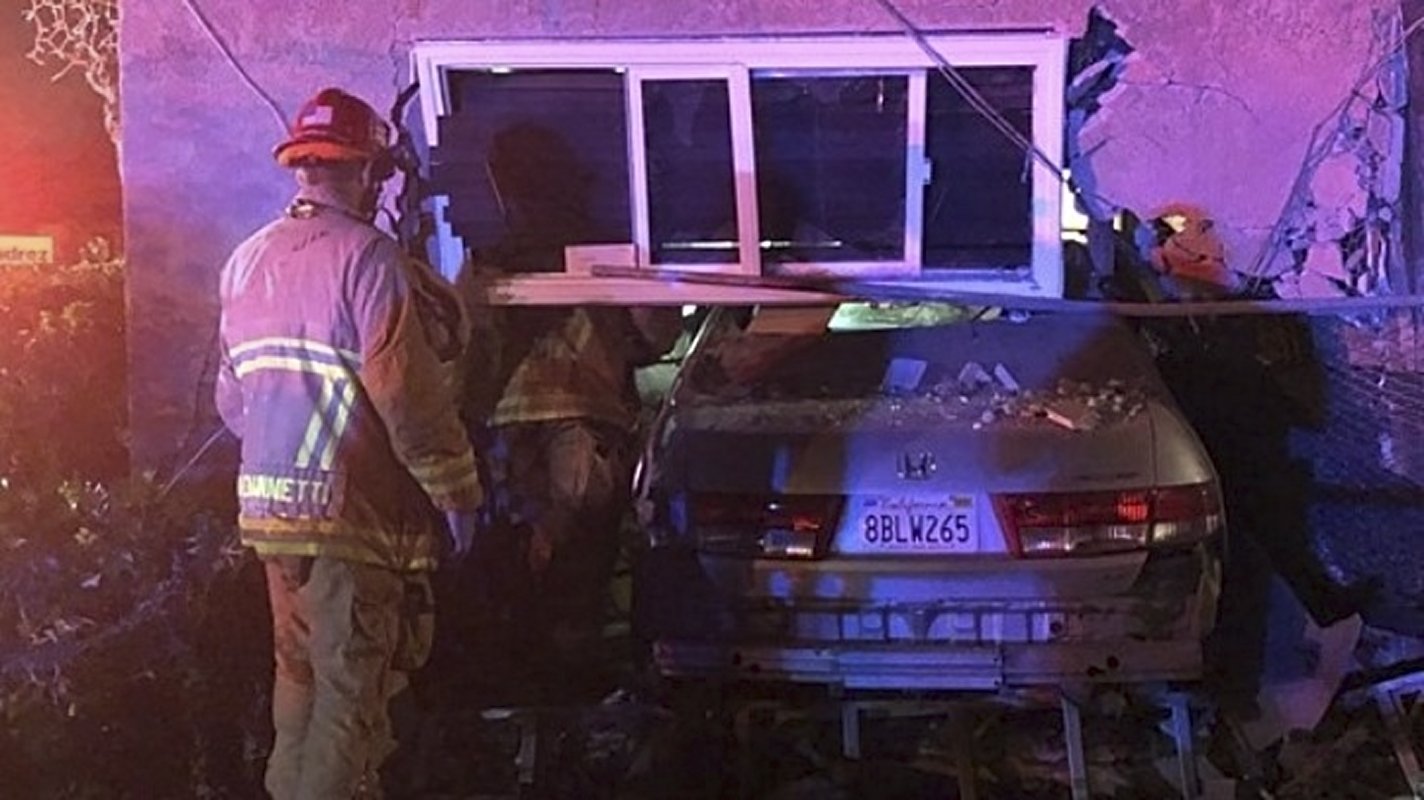 A car half sticking out of the home in Riverside, CA, it plowed into, as firefights inspect the wreckage.