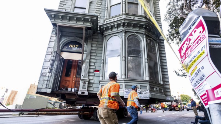 Workers pass a Victorian home as a truck pulls it through San Francisco