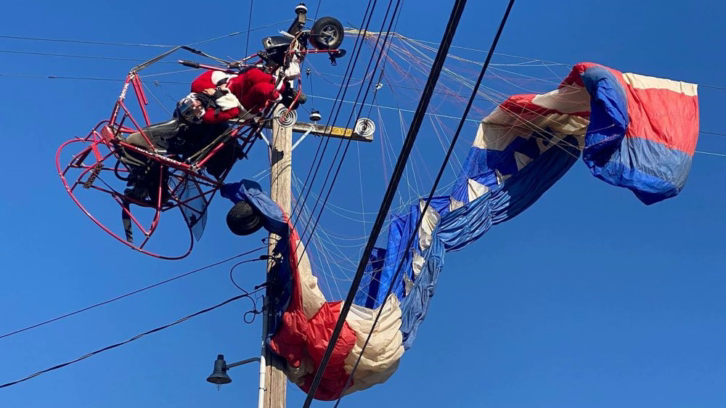 A man dressed as Santa Claus who was flying on a powered parachute on his way to deliver candy canes to children is seen stuck on power lines